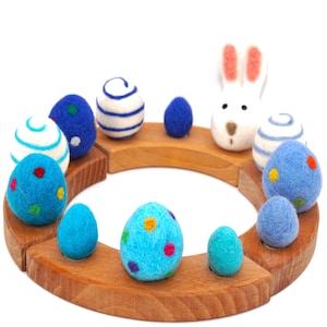 May include: A wooden Easter egg display with felt eggs in blue, teal, and white, some with polka dots and stripes. A white felt bunny with pink ears is also included. The display sits on a wooden circular base. The eggs are in various sizes.