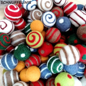 Könnte beinhalten: Eine Sammlung bunter Filzkugeln in verschiedenen Größen und Designs. Die Kugeln weisen Streifen, Wirbel und unifarbene Muster auf, darunter Rot, Weiß, Grün, Blau, Braun und Gelb. Der Text "SCHNUFFELINIS" ist sichtbar.