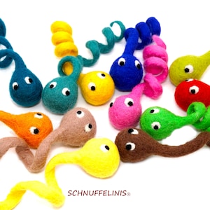 Könnte beinhalten: Ein Set mit 12 bunten Filz-Kaulquappen mit schwarzen Augen. Jede Kaulquappe hat einen gekräuselten Schwanz und ist in einer anderen Farbe, darunter Rot, Orange, Gelb, Grün, Blau und Lila.