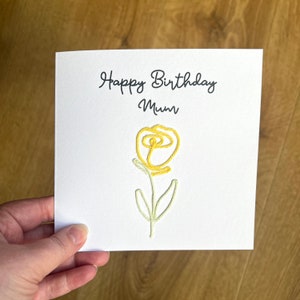 Peut inclure: Une carte blanche avec le texte "Happy Birthday Mum" et une fleur brod&eacute;e jaune.