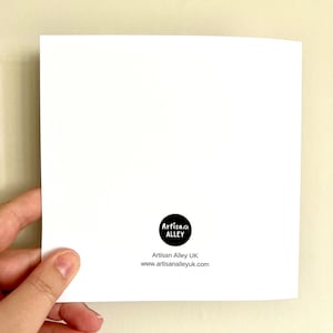 May include: A white card held in a hand, with a black circular logo reading "Artisan Alley". Below the logo is "Artisan Alley UK" and the website address www.artisanalleyuk.com.