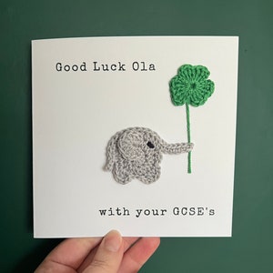 May include: A white card with the text "Good Luck Ola with your GCSE's". A crocheted gray elephant holding a green four-leaf clover.