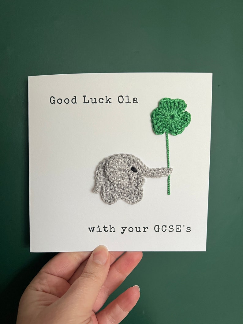 May include: A white card with the text "Good Luck Ola with your GCSE's". A crocheted gray elephant holding a green four-leaf clover.