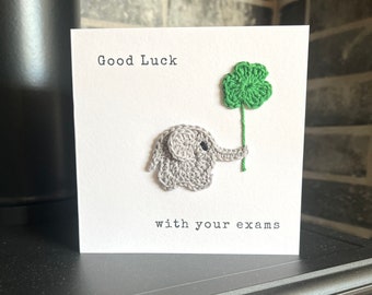 May include: A white card with the text "Good Luck with your exams" and a crocheted grey elephant holding a green four-leaf clover.