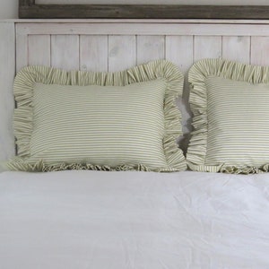 May include: Two green and white striped pillowcases with ruffled edges on a white bed.