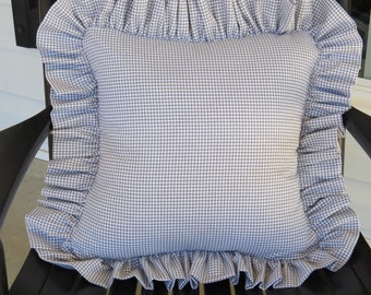 May include: A blue and white gingham pillow with a ruffled edge. The pillow is sitting on a black chair.