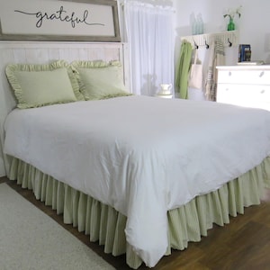 May include: A white bed with a green and white striped bed skirt and matching pillowcases. The headboard has a sign that says "grateful".