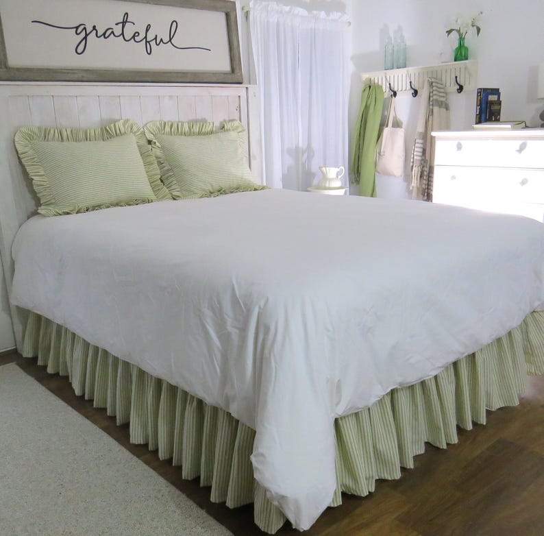May include: A white bed with a green and white striped bed skirt and matching pillowcases. The headboard has a sign that says "grateful".