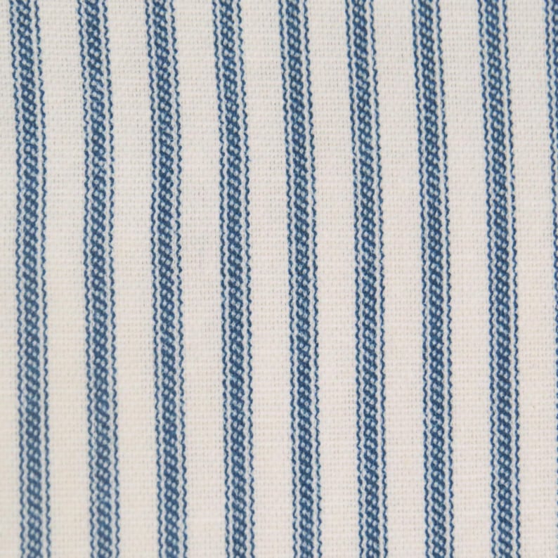 May include: Close-up of a fabric with vertical blue stripes on a white background. The stripes are evenly spaced and have a textured appearance, creating a classic, timeless pattern. The fabric appears to be cotton or a similar material.