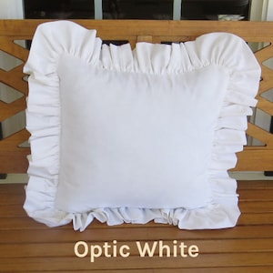 May include: White pillow with a ruffled edge. The pillow is sitting on a wooden surface. Optic White.