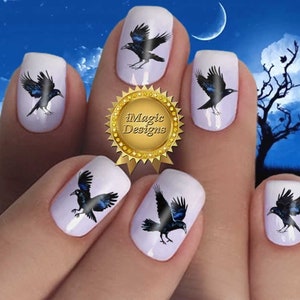 May include: Black crow nail decals on white painted fingernails. The decals are a realistic depiction of a crow in flight. The image includes the text "iMagic Designs".