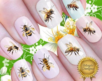 Op de afbeelding: Nagelstickers met realistische illustraties van honingbijen op lichtroze en witte vingernagels. Elke nagel toont een gedetailleerde bij met gele en zwarte strepen en doorschijnende vleugels. Een gouden zegel bevat de tekst iMagic Designs.