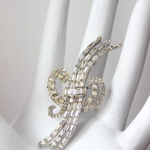 May include: A silver and crystal brooch with a swirling design. The brooch is made of baguette-shaped crystals and round crystals.
