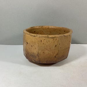 May include: A brown ceramic bowl with a textured surface. The bowl has a rounded shape and a slightly flared rim.