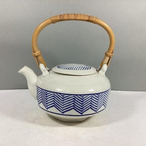 May include: A white ceramic teapot with a blue and white geometric pattern. The teapot has a bamboo handle and a lid.