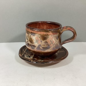 May include: A brown and white ceramic teacup and saucer set with a geometric pattern. The cup has a handle and the saucer is round.