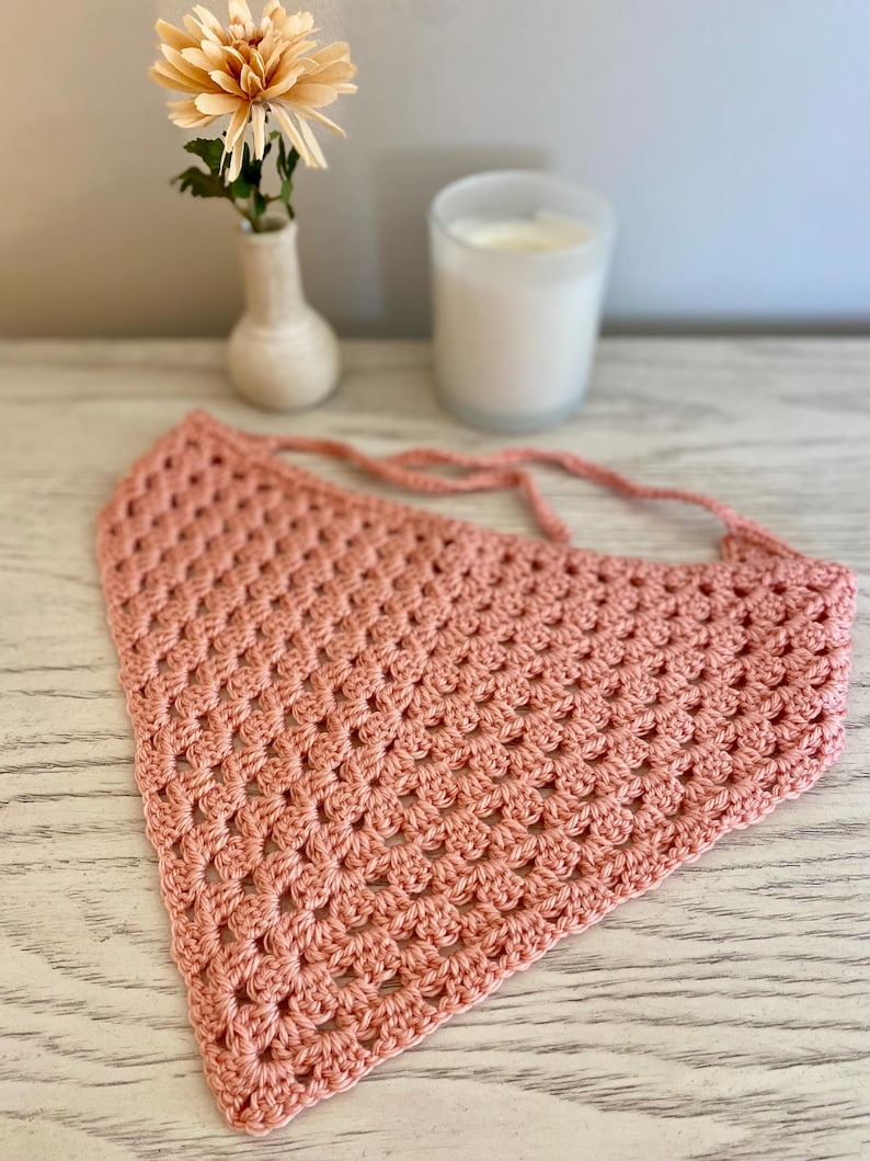 A peach crocheted bandana lays on a dresser. This boho style hair scarf has a delicate open stitch pattern.