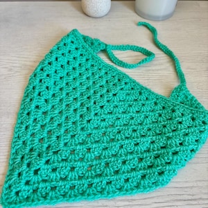 May include: A bright green triangular crochet bandana featuring a classic granny square stitch pattern. The accessory is crafted from yarn and includes two long, thin crocheted ties at the top corners for securing the piece around the head or neck.