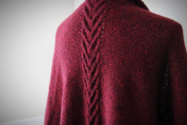 Puede incluir: Un chal de punto burdeos con un patr&oacute;n de trenzas en la espalda.