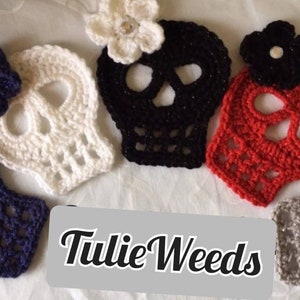 May include: Five crocheted skull ornaments with flowers. The skulls are white, black, red, gray, and navy blue. The flowers are white, black, and red. The text "Tulie Weeds" is visible in the image.