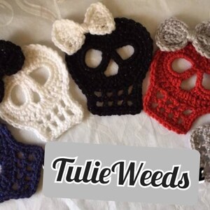 May include: Five crocheted skull ornaments with bows in various colors, including white, black, red, gray, and blue. The skulls are all the same size and shape, and they have a delicate, lacy design. The bows are all different colors and styles, and they add a touch of whimsy to the ornaments. The text "Tillie Weeds" is visible in the image.