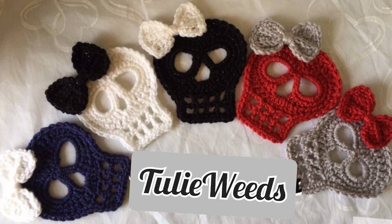 May include: Five crocheted skull ornaments with bows in various colors, including white, black, red, gray, and blue. The skulls are all the same size and shape, and they have a delicate, lacy design. The bows are all different colors and styles, and they add a touch of whimsy to the ornaments. The text "Tillie Weeds" is visible in the image.