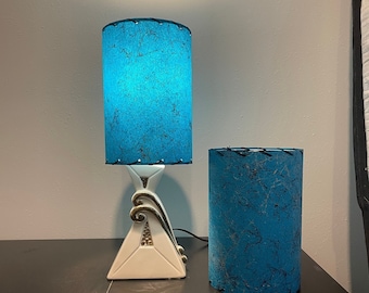 May include: A vintage table lamp with a turquoise blue cylindrical shade and a matching lampshade. The lamp has a white triangular base with gold accents. The shades have a textured pattern.