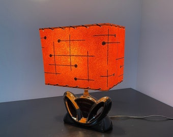 May include: A mid-century modern table lamp with a black ceramic base and a square orange lampshade with a geometric pattern.