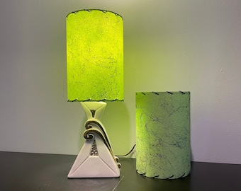 May include: Two green lampshades with a white ceramic lamp base. The lampshades are made of a textured material and have a green and white pattern. The lamp base is a triangular shape with a gold trim.