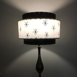 May include: A black and white table lamp with a double-tiered shade featuring a starburst pattern. The lamp has a black base with a gold accent.