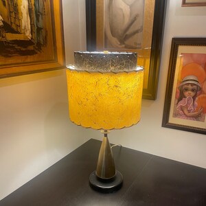 May include: A vintage table lamp with a gold and black patterned lampshade. The lamp has a gold metal base and a black base.