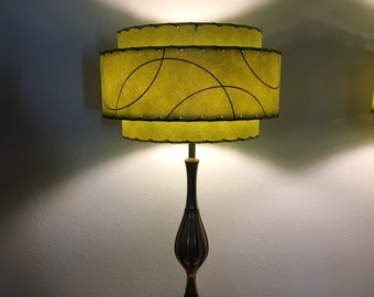 May include: A mid-century modern table lamp with a green, two-tiered lampshade featuring a black abstract design. The lamp has a dark wood base with a slender, vase-like shape.