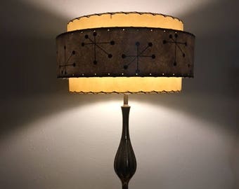 May include: A mid-century modern table lamp with a black and brown ceramic base and a two-tiered lampshade. The lampshade is beige with a brown band featuring a geometric pattern of black stars and dots.