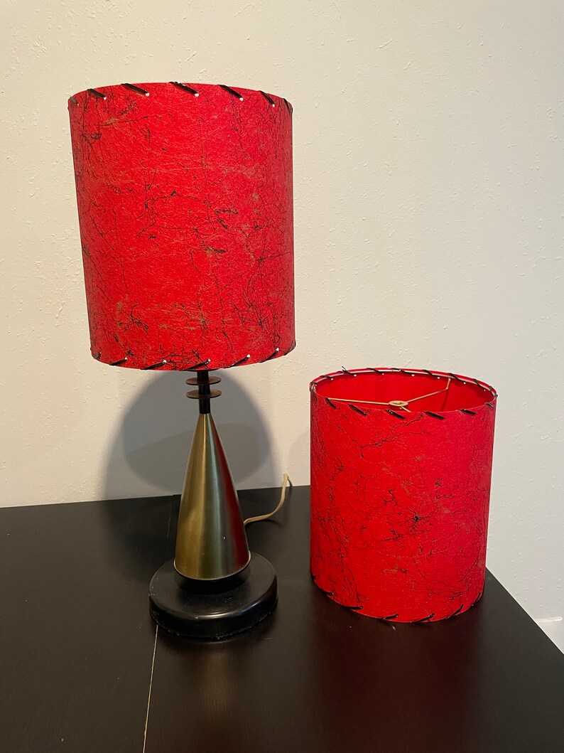 May include: Two red lampshades with black stitching and a black and gold lamp base. The lampshades are made of a textured fabric.