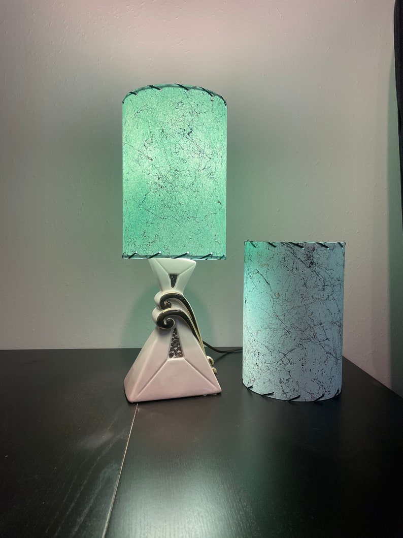 Op de afbeelding: Twee vintage lampen met groene en witte gepatroneerde lampenkappen. De lamp aan de linkerkant heeft een witte keramische voet met gouden accenten. De lamp aan de rechterkant heeft een witte keramische voet.