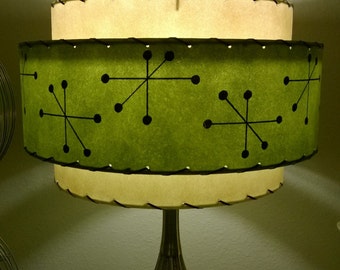 May include: A two-tiered lampshade with a green bottom tier and a cream top tier. The green tier has a black geometric pattern of stars. The lampshade is attached to a silver metal lamp base.