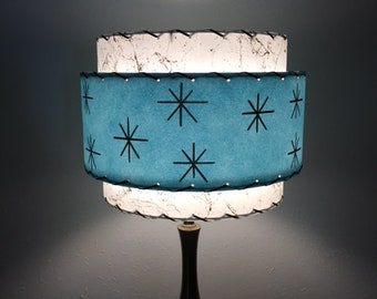 May include: A mid-century modern lamp with a blue and white shade featuring a starburst pattern. The lamp has a black base.