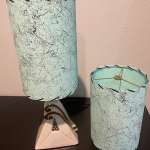 Op de afbeelding: Twee vintage tafellampen met een witte keramische voet en een lichtblauwe lampenkap met patroon. De lampenkappen hebben zwarte stiksels rond de randen.