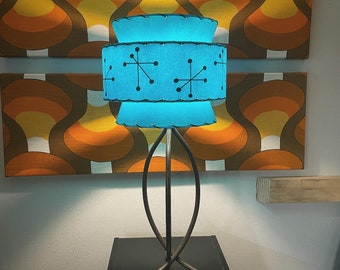 May include: A blue and black mid-century modern lamp with a starburst design on the shade. The lamp is on a black metal stand with a tripod base.