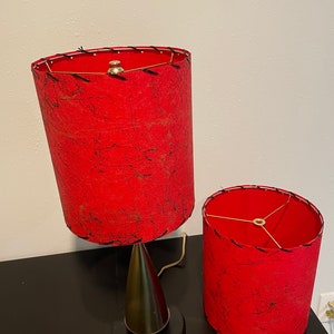 May include: Two red lampshades with black stitching and a gold metal base. The lampshades are made of a textured fabric.