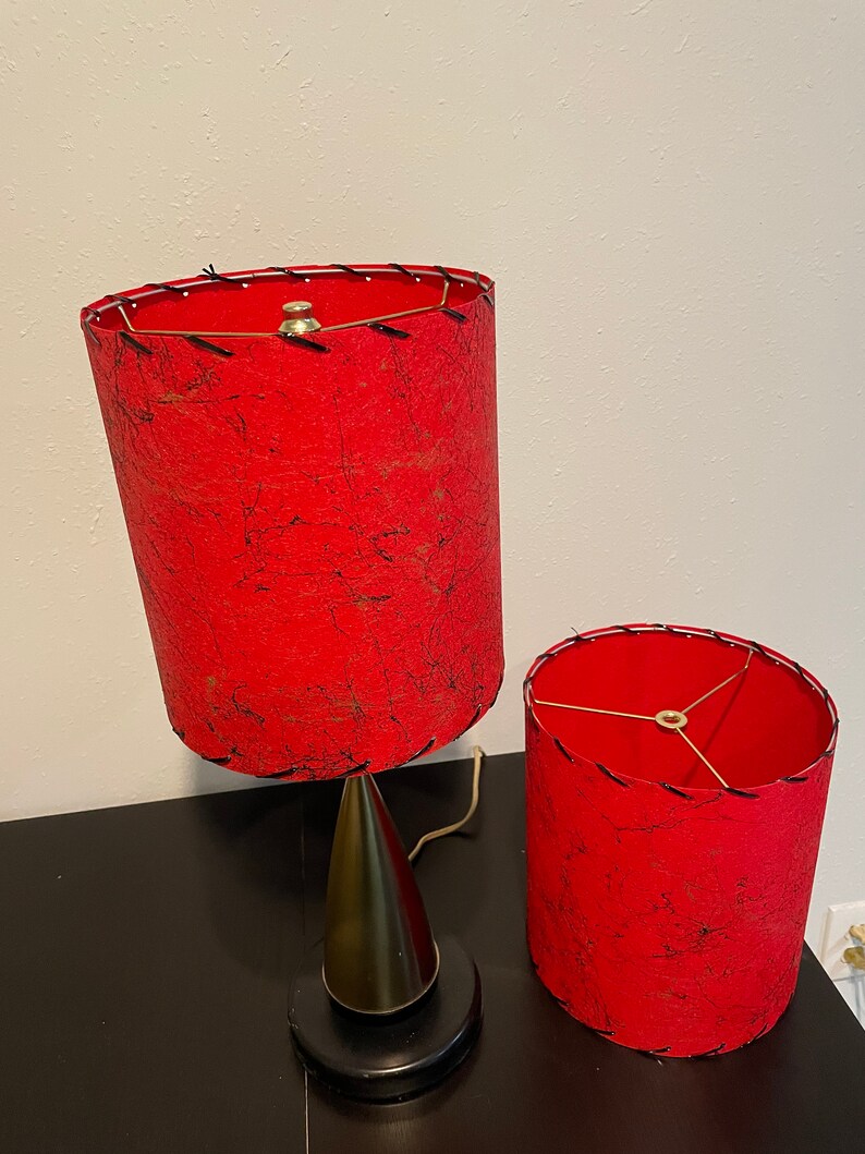 May include: Two red lampshades with black stitching and a gold metal base. The lampshades are made of a textured fabric.