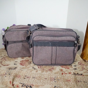 Peut inclure: Deux sacs de voyage Samsonite en tweed brun et gris avec des sangles et des fermetures éclair noires. Le plus grand sac porte le logo Samsonite sur le devant.