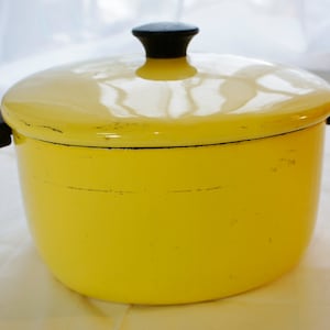 May include: A yellow enamel pot with black handles and a lid. The pot has a worn, vintage look.