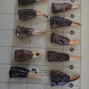 May include: Ten carved objects with a dark brown, textured base and a light-coloured, pointed tip. The objects are arranged on a grid, with the text "This mat is manufactured from 100% pol..." visible.
