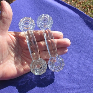 May include: Four clear glass cabinet knobs and pulls. Two knobs are round with a floral design, and two pulls have a similar floral design on the base and a curved handle. The glass is transparent and reflects light.