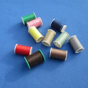 May include: Assortment of colorful thread spools in various shades of red, yellow, green, blue, brown, and gray. The spools are arranged on a blue surface.