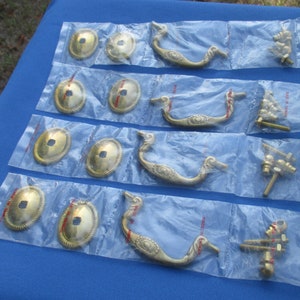 May include: Four sets of gold-toned cabinet hardware, each set includes a decorative pull handle, two oval-shaped knobs, and mounting screws. The handles have a swan-like design.