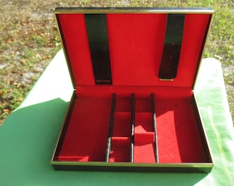 May include: Black and gold jewelry box with red velvet lining and a black felt divider. The box has the word "Buxton" printed on the inside.