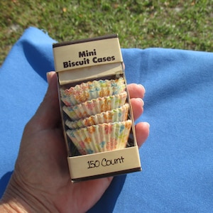 May include: A box of mini biscuit cases, each with a floral pattern in pastel colors. The box is tan with the words "Mini Biscuit Cases" and "150 Count" printed on it.