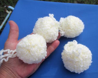 May include: Four white fluffy pom poms, three are on a blue surface and one is being held in a hand.